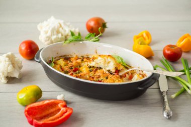 Peynirin altında tatlı biber ve sebzeyle pişirilmiş karnabahar, seramik bir kabın içinde.