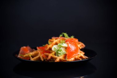 Sebze patatesli waffle ve hafif tuzlu kırmızı balık tabakta, siyah arka planda izole edilmiş..