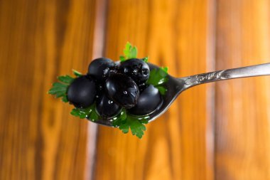 black olives in a spoon on wooden table clipart