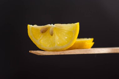 Siyah arka planda izole edilmiş ahşap spatulada taze sulu bir limon dilimi..
