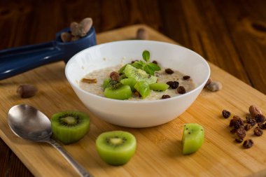 cooked oatmeal with kiwi, honey and nuts in a bowl on a wooden table. clipart