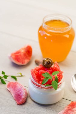 homemade sweet yogurt in a glass jar with pieces of red ripe grapefruit and honey, on a wooden table . clipart