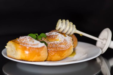 Pişmiş mallar. Süzme peynirli tatlı çörekler ve siyah arka planda izole edilmiş bir tabakta bal. .