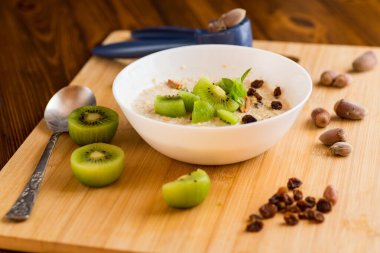 Yulaf ezmesi, kivi, bal ve fındık, ahşap bir masada..