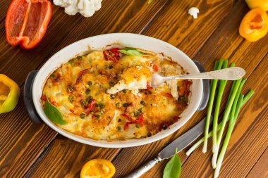 Peynirin altında tatlı biber ve sebzeyle pişirilmiş karnabahar, seramik bir kabın içinde.