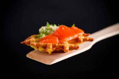 Sebzeli patatesli waffle ve az tuzlu kırmızı balık, siyah arka planda izole edilmiş spatula.