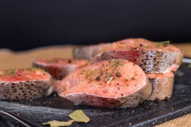 Siyah arka planda baharat ve bitkilerle dolu doğal bir somon parçası..