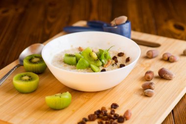 Yulaf ezmesi, kivi, bal ve fındık, ahşap bir masada..