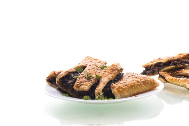 Beyaz arka planda izole bir tabakta mantarlı puf böreği ve susam tohumları..