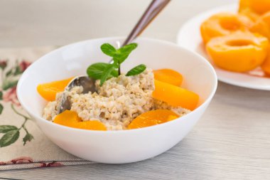 Beyaz kâse içinde şeftali kokulu yulaf ezmesi..