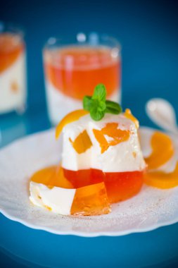 Mavi arka planda şeftali parçalarıyla parlak jöle ve süt jölesi.