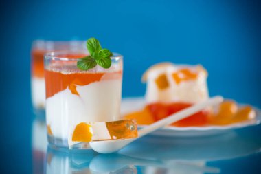 Mavi arka planda şeftali parçalarıyla parlak jöle ve süt jölesi.