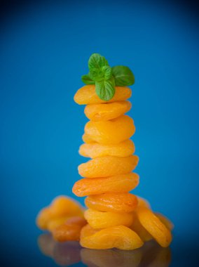 Bir avuç parlak turuncu kurutulmuş kayısı ve mavi arka planda bir tutam nane. .