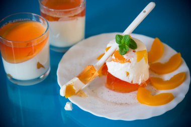 Mavi arka planda şeftali parçalarıyla parlak jöle ve süt jölesi.