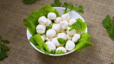 Beyaz kasede mini mozzarella ve gri arka planda yeşiller. Üst görünüm.