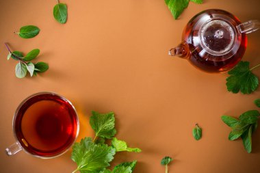 Frenk üzümü yapraklı yeşil çay, cam çaydanlıkta nane ve kahverengi arka planda fincan. Üst görünüm .