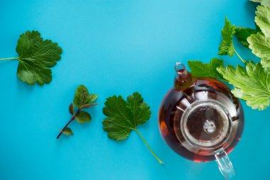 Frenk üzümü yapraklı yeşil çay ve cam çaydanlıkta nane ve mavi arka planda fincan. Üst görünüm .