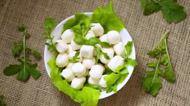Beyaz kasede mini mozzarella ve gri arka planda yeşiller. Üst görünüm.