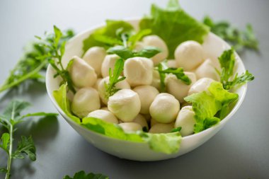 Mini mozzarella topları ve gri arka planda beyaz kasede otlar..