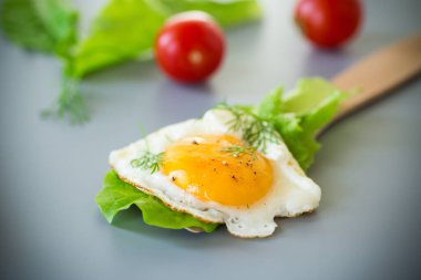 Gri arka planda yağda yumurta ve taze salata yapraklarıyla ev yapımı kahvaltı..