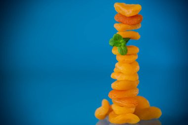 Bir avuç parlak turuncu kurutulmuş kayısı ve mavi arka planda bir tutam nane..