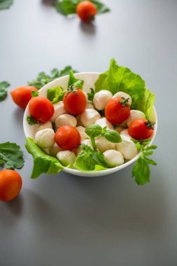 Mini mozarellalı beyaz kase ve gri arka planda yeşiller..