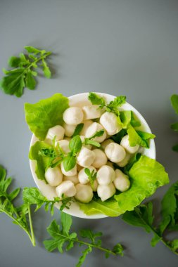 Üzerinde mini mozarella ve taze bitkiler olan beyaz kase..