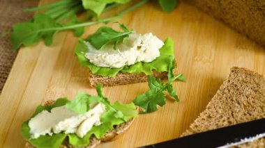 Peynirli çavdar ekmeği dilimi ve masada yeşillikler.