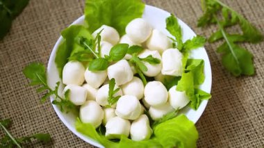 Beyaz kasede mini mozzarella ve gri arka planda yeşiller. Üst görünüm.