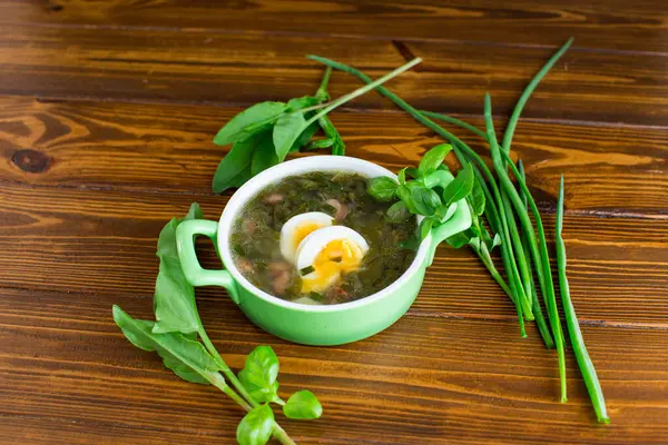 Koyu ahşap bir masa üzerinde yeşil ve yumurtalı Ukrayna çorbası..