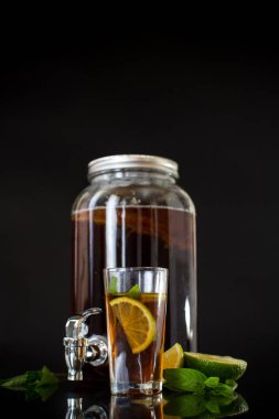 Cam bir kavanozda kombu çayı tazeliyorum ve siyah arka planda limon dolu bir bardak..