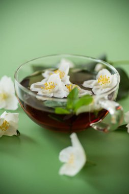 Yeşil arka planda cam bir kapta kokulu yasemin çayı.