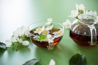 Yeşil arka planda cam bir kapta kokulu yasemin çayı.