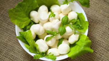 Beyaz kasede mini mozzarella ve gri arka planda yeşiller. Üst görünüm.