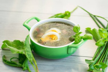 Yeşil sebzeli Ukrayna çorbası ve açık ahşap masa üzerinde yumurta..