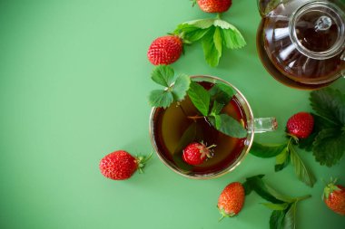 Yeşil arka planda şeffaf cam kaplı parlak çilek çayı..