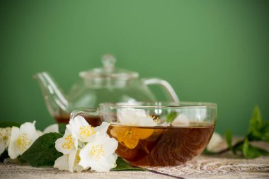 Yeşil arka planda cam çaydanlıkta yaseminli yeşil çay..