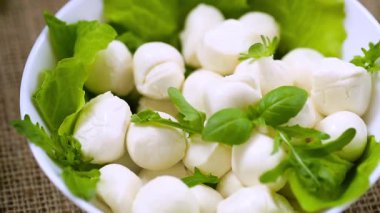 Beyaz kasede mini mozzarella ve gri arka planda yeşiller. Üst görünüm.