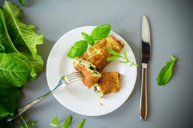 Beyaz bir tabağın üstünde yeşillikler olan omlet rulosu..