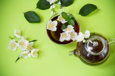 Yeşil arka planda cam bir kapta kokulu yasemin çayı.