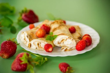 Süzme peynirli tatlı krepler ve yeşil arka planda çilekler..