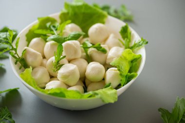 Beyaz kasede mini mozzarella ve gri arka planda yeşiller. Üst görünüm.