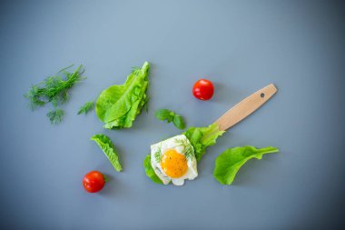 Gri arka planda yağda yumurta ve taze salata yapraklarıyla ev yapımı kahvaltı..