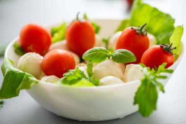 Beyaz kâse içinde mini mozzarella otlar ve kiraz domatesleri..