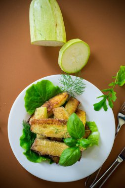 Kahverengi arka planda beyaz tabakta ev yapımı kızarmış kabak..