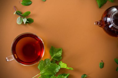 Frenk üzümü yapraklı yeşil çay, cam çaydanlıkta nane ve kahverengi arka planda fincan. Üst görünüm .