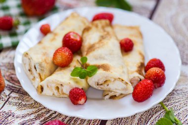 Süzme peynirli krep ve ahşap bir masanın üstünde çilek..