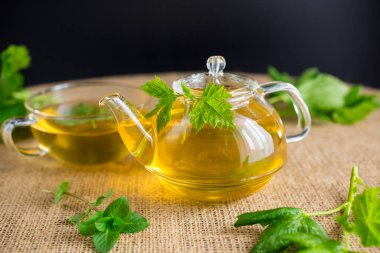 Frenk üzümü yapraklı yeşil çay ve cam çaydanlıkta nane ve siyah arka planda fincan..