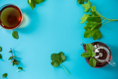 Frenk üzümü yapraklı yeşil çay ve cam çaydanlıkta nane ve mavi arka planda fincan. Üst görünüm .