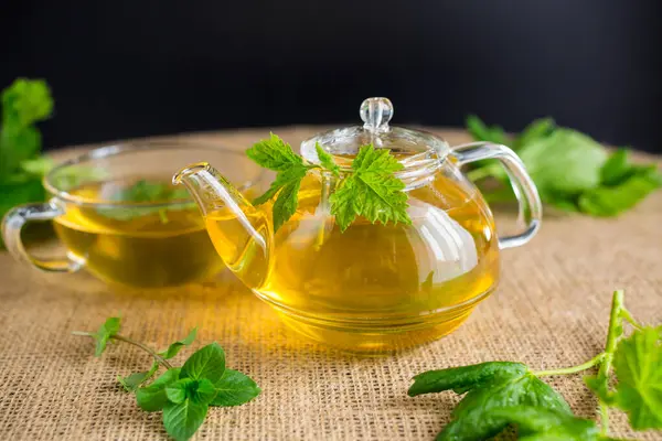 Frenk üzümü yapraklı yeşil çay ve cam çaydanlıkta nane ve siyah arka planda fincan..
